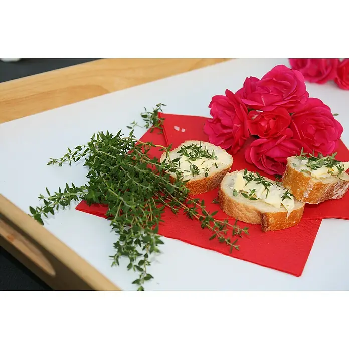 Blu Bio Rosenthymian - Thymus ssp., Topfgröße: 12 cm - Stillleben mit Baguettescheiben mit Butter und Thymian, roten Rosen und einem roten Tuch auf einem weißen Teller.