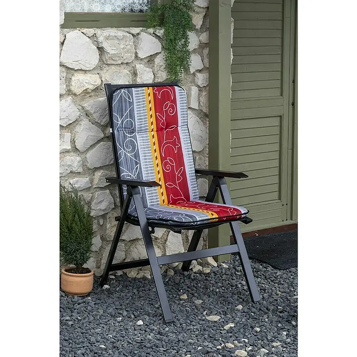 beo Gartenmöbel-Auflage Elmira - Hochlehner, 6 Stk., L x B x H: 114 x 47 x 5 cm, Baumwolle, Polyester, Rot/Orange/Grau - Das Bild zeigt einen stilvollen, schwarzen Gartenstuhl mit einer bunt gemusterten Auflage vor einer Steinwand und einer grünen Tür.