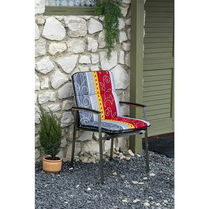 beo Gartenmöbel-Auflage Elmira - Niederlehner, 6 Stk., L x B x H: 96 x 47 x 5 cm, Baumwolle, Polyester, Rot/Grau/Gelb - Gartenstuhl mit buntem Polster vor einer Steinwand und grüner Tür. Die Polsterung ist rot, gelb und grau gemustert für Komfort im Freien.