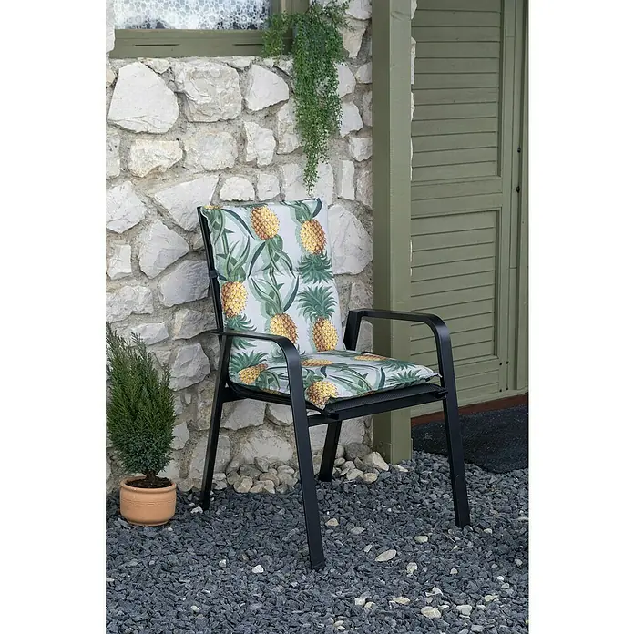 beo Gartenmöbel-Auflage Treffelstein - Niederlehner, 2 Stk., L x B x H: 98 x 46 x 8 cm, Baumwolle, Polyester, Grün/Gelb - Nahaufnahme eines schwarzen Gartenstuhls mit Ananasmuster-Kissen vor einer Steinmauer.