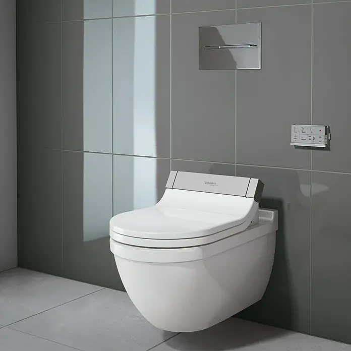 Duravit Starck 3 Wand-WC Typ 2 - Mit Spülrand, Ohne Spezialglasur, Spülform: Tief, WC Abgang: Waagerecht, Weiß - Nahaufnahme einer weißen Duravit Duschtoilette mit Fernbedienung und Betätigungsplatte vor grauen Fliesen.