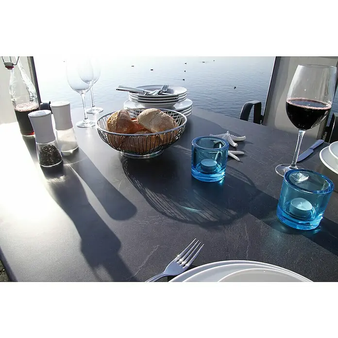 Acamp Gartenmöbel-Set Urban/Acaplan Loft - 5 -tlg., Aluminium, Textil, Klappbar, Anthrazit - Ein Tisch im Freien mit Weingläsern, Geschirr, Brot, Gewürzen, blauen Kerzenhaltern und Seesternen, die eine entspannte Atmosphäre schaffen.