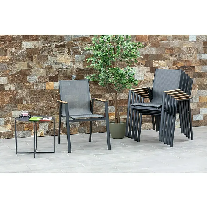 Acamp Stapelsessel Vegas - 6 Stk., Aluminium, Textil, Stapelbar, Anthrazit, B x T x H: 67 x 58 x 88 cm - Gartenmöbel-Set mit Stapelstühlen, einem einzelnen Stuhl und einem kleinen Tisch im Freien vor einer Ziegelwand.