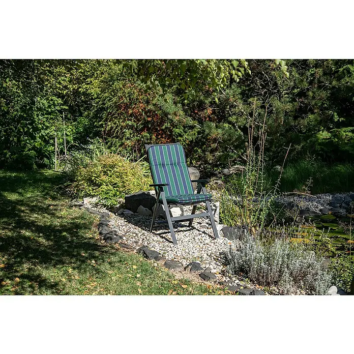 beo Gartenmöbel-Auflage Paselista - Hochlehner, 6 Stk., L x B x H: 114 x 47 x 5 cm, Blau/Grün - Ein Gartenstuhl mit blau-grün gestreiftem Kissen steht auf einem Kiesweg neben einem Teich. Die Szene ist von üppigem Grün umgeben.
