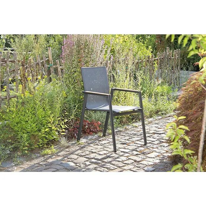 Acamp Gartenmöbel-Set Vegas/Chicago - 7 -tlg., Aluminium, Textil, Grau - Ein grauer Gartenstuhl mit Armlehnen steht auf einem gepflasterten Weg, umgeben von üppigem Grün und Pflanzen.