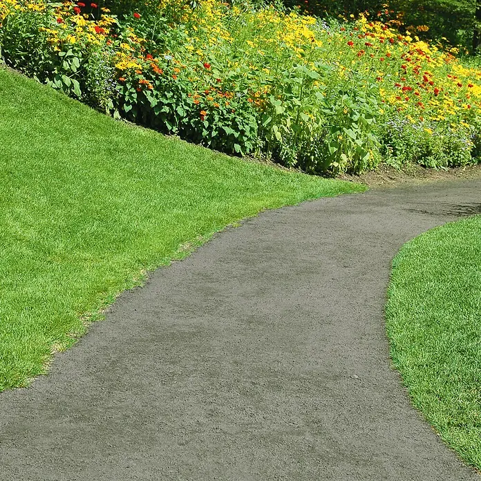 Dansand Gartenweg - Anthrazit, 20 kg - Ein geschwungener, dunkelgrauer Gartenweg schlängelt sich durch einen üppigen Garten mit bunten Blumen und saftig grünem Gras.
