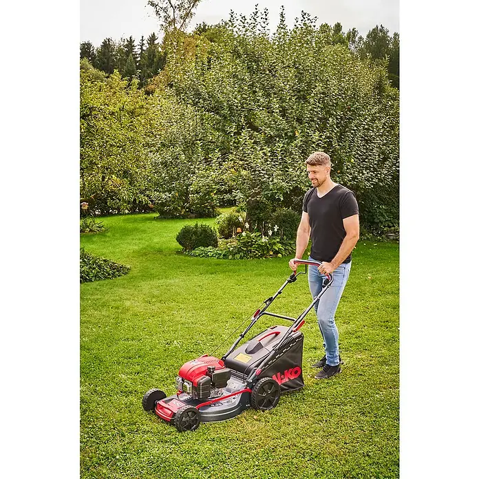 AL-KO Benzin-Rasenmäher Easy 4.66 SP-D - 2,4 kW, 149 cm³, Schnittbreite: 46 cm - Ein Mann mäht den Rasen mit einem AL-KO Benzinrasenmäher in einem üppigen Garten. Das Gerät ist rot-schwarz und gut sichtbar.