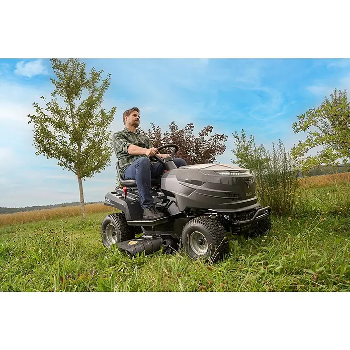 AL-KO Easy Rasentraktor 13-92.6 CS-A - 7,2 kW, Schnittbreite: 92 cm, Schnitthöhe: 30 mm - 90 mm, Kraftstoffart: Benzin - Mann auf AL-KO Aufsitzmäher, der auf einer grünen Wiese fährt. Der Aufsitzmäher ist grau und hat einen modernen Look.
