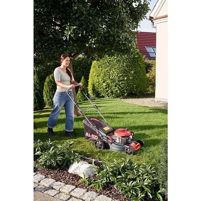 AL-KO Benzin-Rasenmäher Easy 4.16 P-D - 1,2 kW, 79,8 cm³, Schnittbreite: 41 cm - Eine Frau mäht den Rasen mit einem AL-KO Benzinrasenmäher in ihrem Garten, umgeben von üppigem Grün und Sträuchern.