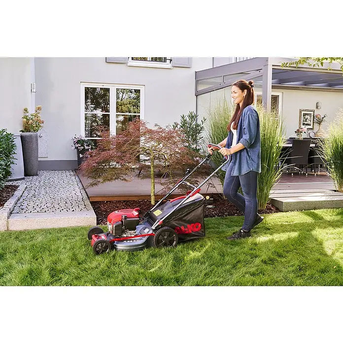 AL-KO Benzin-Rasenmäher Easy 4.66 P-D - 1,9 kW, 131 cm³, Schnittbreite: 46 cm - Frau mäht Rasen mit einem AL-KO Benzinrasenmäher. Der Rasenmäher hat einen roten Motor und einen schwarzen Fangkorb.