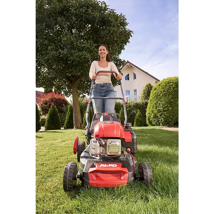 AL-KO Benzin-Rasenmäher Easy 4.26 P-D - 1,9 kW, 131 cm³, Schnittbreite: 41 cm - Eine Frau bedient einen roten AL-KO Rasenmäher in einem grünen Garten mit Bäumen und einem Haus im Hintergrund.
