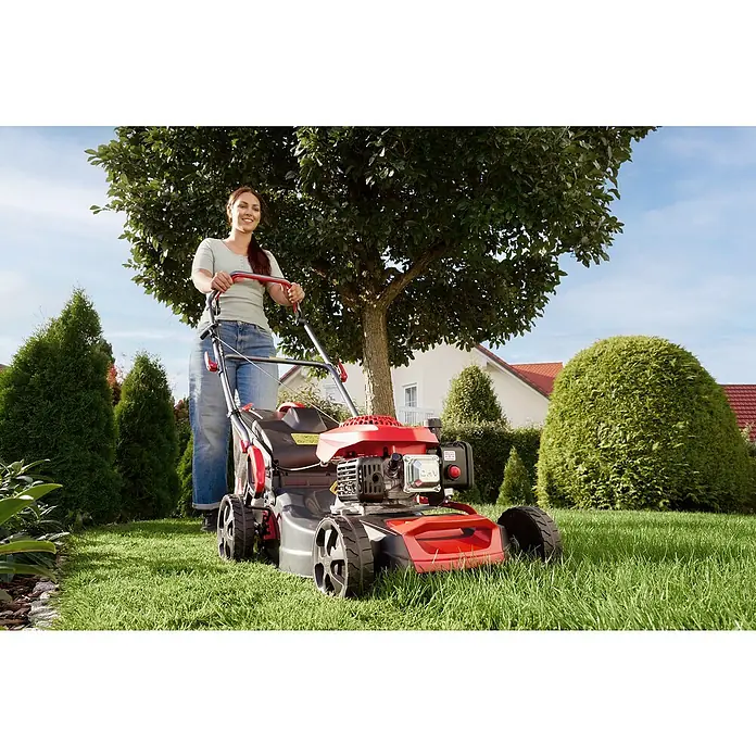 AL-KO Benzin-Rasenmäher Easy 4.16 P-D - 1,2 kW, 79,8 cm³, Schnittbreite: 41 cm - Eine Frau bedient einen roten Rasenmäher im Garten. Der Rasenmäher ist das Hauptprodukt, umgeben von Grün und einem Haus im Hintergrund.