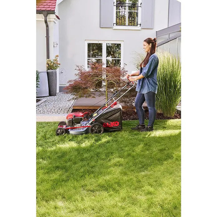 AL-KO Benzin-Rasenmäher Easy 4.66 P-D - 1,9 kW, 131 cm³, Schnittbreite: 46 cm - Eine Frau mäht den Rasen mit einem roten AL-KO Rasenmäher in einem grünen Garten neben einem Haus.