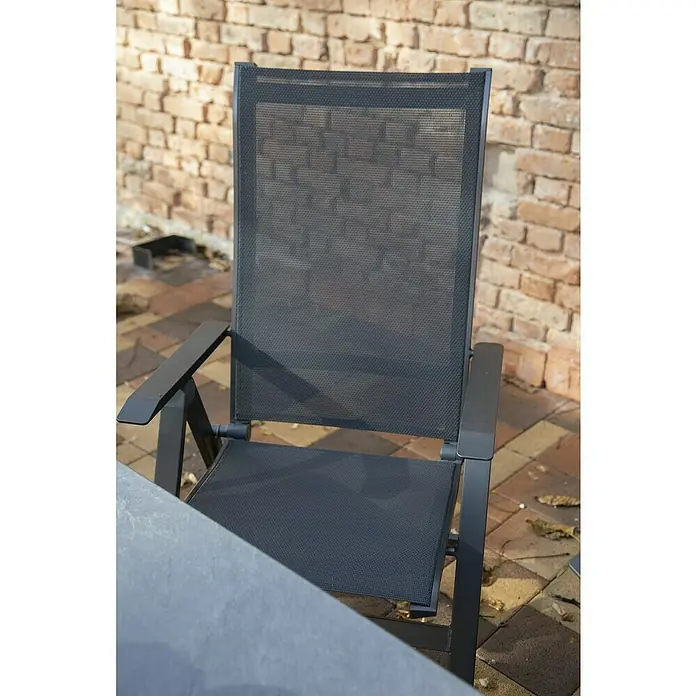 Acamp Gartenmöbel-Set Urban/Extensio - 7 -tlg., Aluminium, HPL, Schwarz - Nahaufnahme eines schwarzen Gartensessels mit Netzbespannung vor einer Ziegelwand.