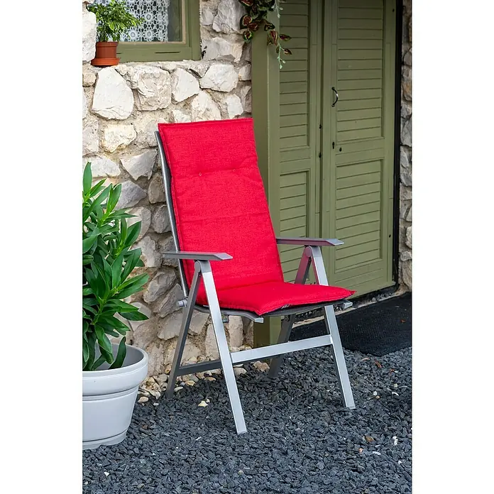 beo Gartenmöbel-Auflage Gera - Hochlehner, 6 Stk., L x B x H: 120 x 48 x 5 cm, Baumwolle, Polyester, Blau/Rot - Einladender roter Gartensessel vor einer rustikalen Steinmauer und einer grünen Tür, der zum Entspannen im Freien einlädt.