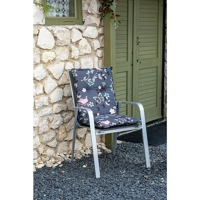 beo Gartenmöbel-Auflage Bregenz - Niederlehner, 6 Stk., L x B x H: 101 x 50 x 6 cm, Baumwolle, Polyester, Anthrazit/Rosa - Ein grauer Gartenstuhl mit Blumenmuster-Kissen steht vor einer Steinmauer und einer grünen Tür.