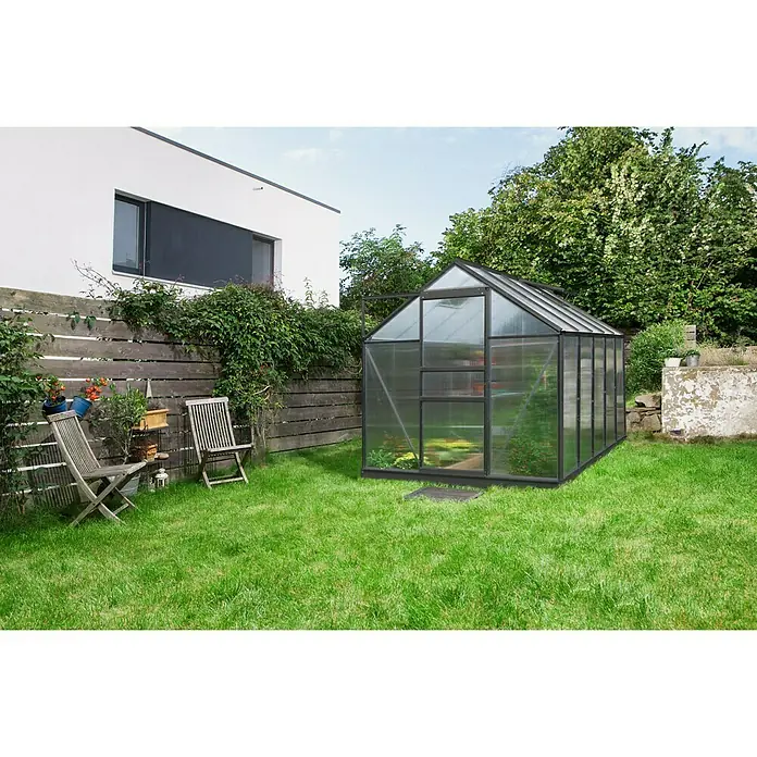Vitavia Gewächshaus Venus 6200 - Außenmaß inkl. Dachüberstand (B x T): 195 x 321 cm, 6 mm, Schwarz - Ein Gewächshaus mit schwarzem Rahmen steht in einem grünen Garten neben einem modernen Haus und einem Holzzaun.