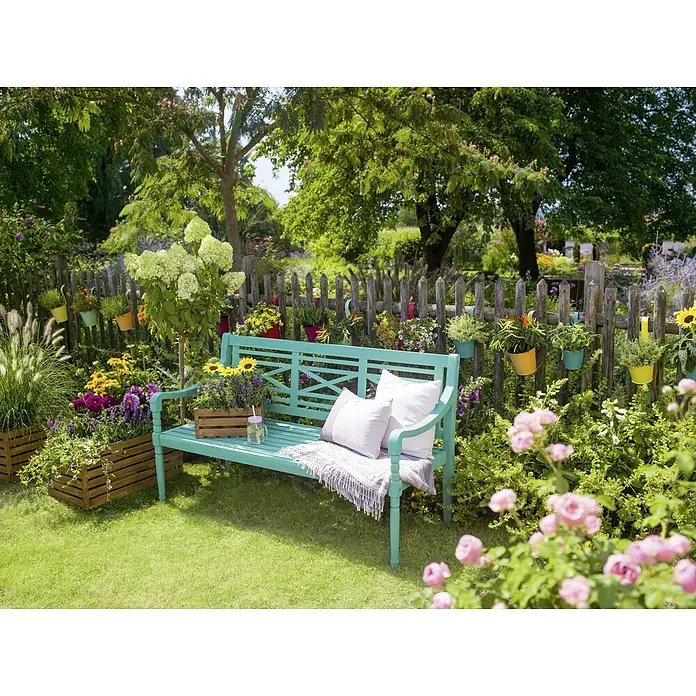 Sunfun Gartenbank Alea - B x T x H: 150 x 62 x 87 cm, Akazie, Türkis - Gartenszene mit einer türkisfarbenen Bank, dekoriert mit Kissen und umgeben von üppiger Vegetation und bunten Blumen.