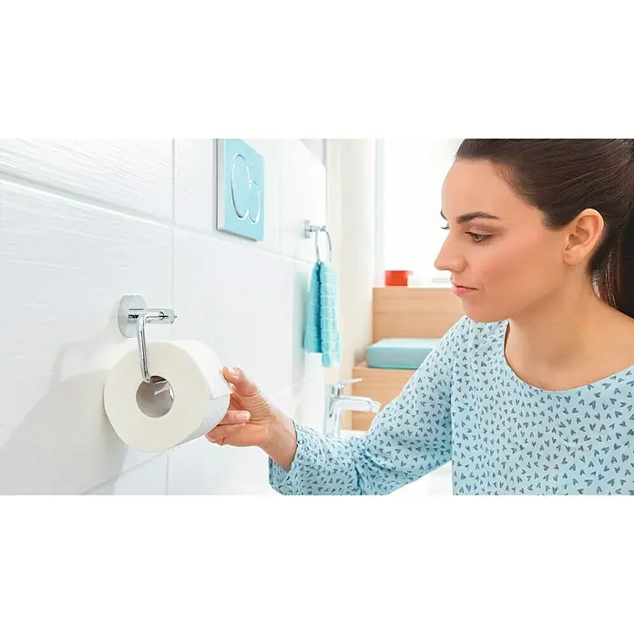 Tesa Smooz Toilettenpapierhalter - Ohne Deckel, Chrom, Glänzend - Frau entnimmt Toilettenpapier aus einem modernen, verchromten Toilettenpapierhalter im Badezimmer mit weißen Fliesen.
