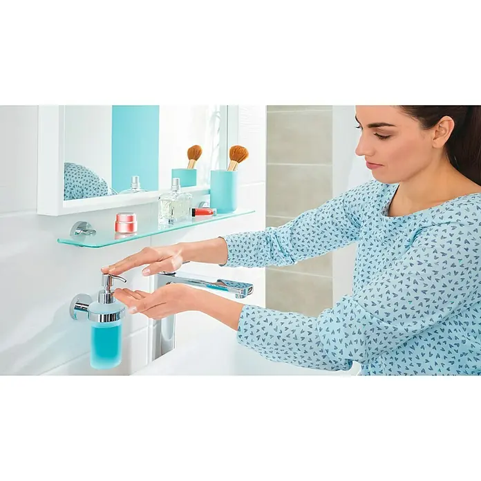 Tesa Smooz Seifenspender - Mit Halterung, Metall, Satiniert/Chrom - Frau benutzt einen Flüssigseifenspender im Badezimmer. Der Seifenspender ist an der Wand montiert und mit blauer Seife gefüllt.