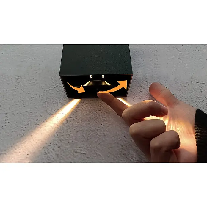 Starlux LED-Außenwandleuchte Effect - 6 W, 10 x 6 x 12 cm, Anthrazit, IP65 - Nahaufnahme einer schwarzen Außenleuchte mit Pfeilen, die die Richtung des Lichtstrahls anzeigen, während eine Hand die Leuchte berührt.