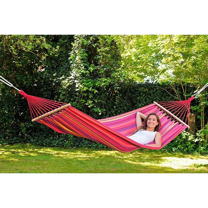 Amazonas Stabhängematte Tonga Vulcano - L x B: 310 x 100 cm, Rot/Orange/Gelb - Frau entspannt in einer farbenfrohen Hängematte im Garten. Perfekt zum Entspannen im Freien, die Hängematte bietet Komfort und Stil.