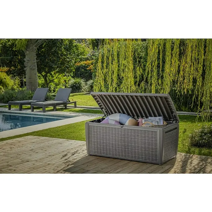 Keter Baúl para jardín Taiwan - L x An x Al: 73 x 145 x 64 cm, Marrón, Plástico - Una caja de almacenamiento Keter gris con aspecto de mimbre se sienta en una cubierta de madera, perfecta para guardar cojines y juguetes.