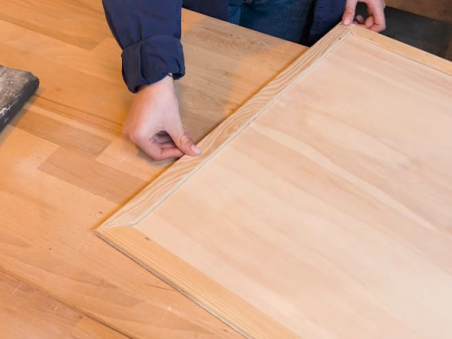 Mit einer Holzplatte und einer Holzleiste wird ein Rahmen zusammengestellt