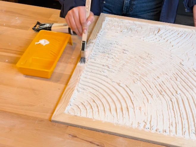 Mit weißer Acrylfarbe wird der Rahmen des selbstgemachten Strukturbildes angemalt