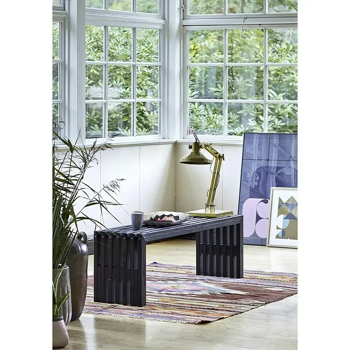 Plus Gartenbank Rustik - B x T x H: 138 x 36 x 45 cm, Nadelholz, Schwarz - Einrichtungsszene mit einer stilvollen schwarzen Holzbank auf einem bunten Teppich, beleuchtet von einer goldenen Lampe.