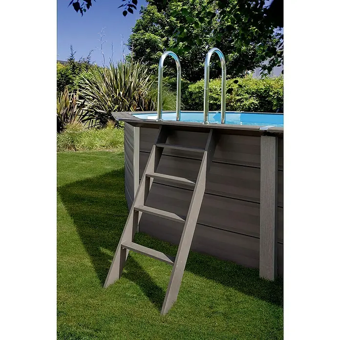 Gre Avantgarde Piscina de WPC KPCOV66 - L x An x Al: 664 x 386 x 124 cm, 21.500 l, Gris oscuro - Primer plano de una escalera de piscina unida a una piscina elevada en un entorno de jardín, con una exuberante vegetación de fondo. La escalera es de madera con pasamanos de metal.