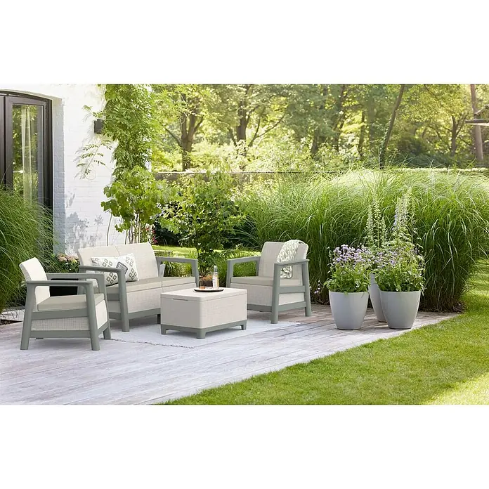 Keter Conjunto de muebles Scandi - Polipropileno, Gris - Acogedora escena de jardín con un elegante conjunto de salón al aire libre en una terraza de madera, rodeada de exuberante vegetación y plantas.