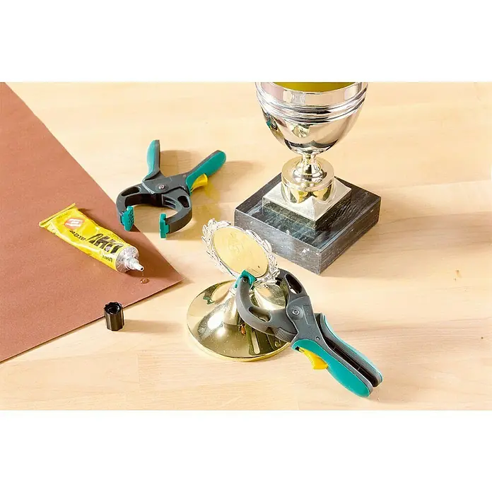 Wolfcraft Ratschenzwinge FZR 30 - Spannweite: 30 mm, Ausladung: 30 mm - Das Foto zeigt eine Nahaufnahme von Werkzeugen zum Basteln, darunter eine Tube Kleber, zwei Klemmen und eine Trophäe.