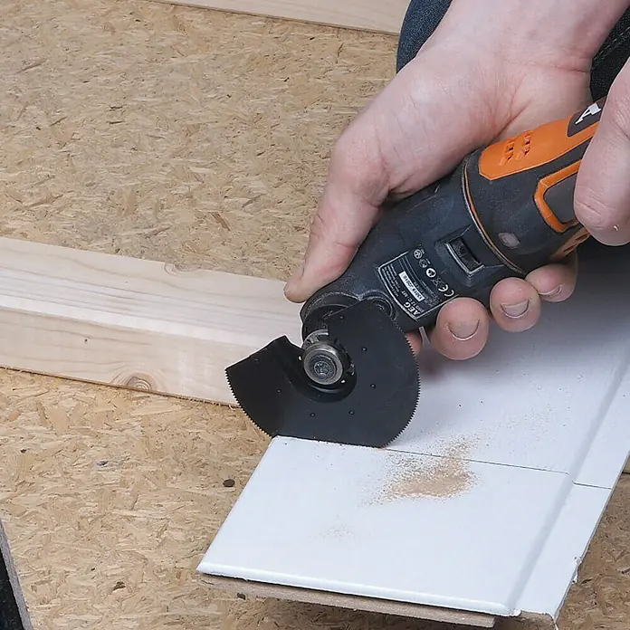 Wolfcraft Sägeblatt für Vibrationssäge halbrund - 85 mm, HS-Stahl - Ein AEG-Multifunktionswerkzeug mit einem runden Sägeblatt schneidet eine weiße Fliese. Staubpartikel sind auf der Oberfläche sichtbar.