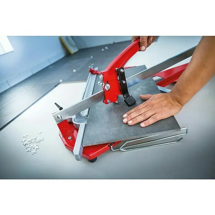Heka Cortador manual de azulejos MagicCut 1200 - Longitud de corte máx.: 1.200 mm, Espesor máx. de azulejo: 20 mm - Un colocador de baldosas está cortando una baldosa gris con un cortador de baldosas. La cortadora de baldosas es roja y plateada, lo que permite cortes precisos.