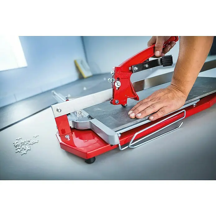 Heka Cortador manual de azulejos MagicCut 1200 - Longitud de corte máx.: 1.200 mm, Espesor máx. de azulejo: 20 mm - Primer plano de una cortadora manual de azulejos roja con una mano que asegura un azulejo. Corte preciso para diseños personalizados.