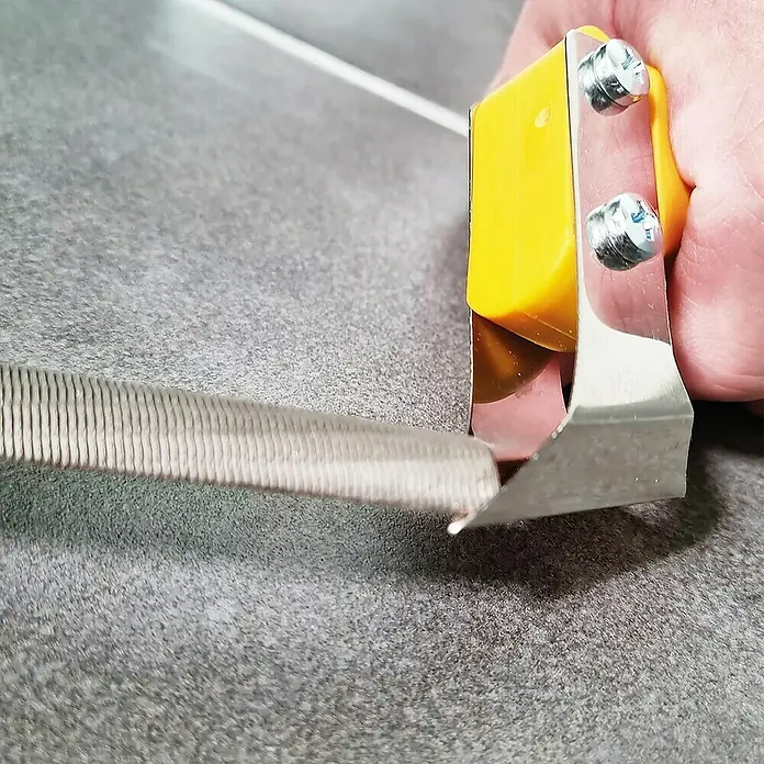 Heka Hoja de repuesto para cuchillas para juntas - Acero para muelle - Primer plano de un cortador de azulejos con mango amarillo que marca un azulejo para crear un borde limpio.