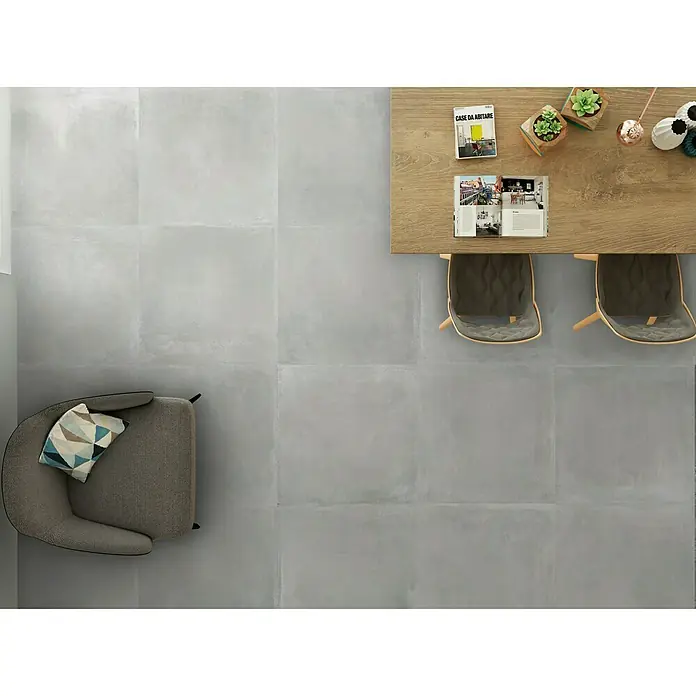 Halcón Pavimento porcelánico Madox - 60 x 60 cm, Gris, Mate, Rectificado, Espesor: 10 mm - Una habitación con suelos de gres gris, un sillón y una mesa con sillas. Su diseño moderno proporciona un ambiente elegante.