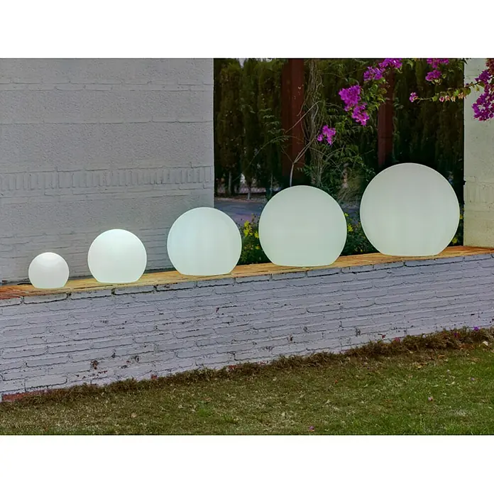 New Garden Solar-Dekoleuchte Buly - Durchmesser: 20 cm, IP65 - Eine Reihe von leuchtenden Gartenkugeln unterschiedlicher Größe stehen auf einer Steinmauer und erhellen den Außenbereich mit sanftem Licht.