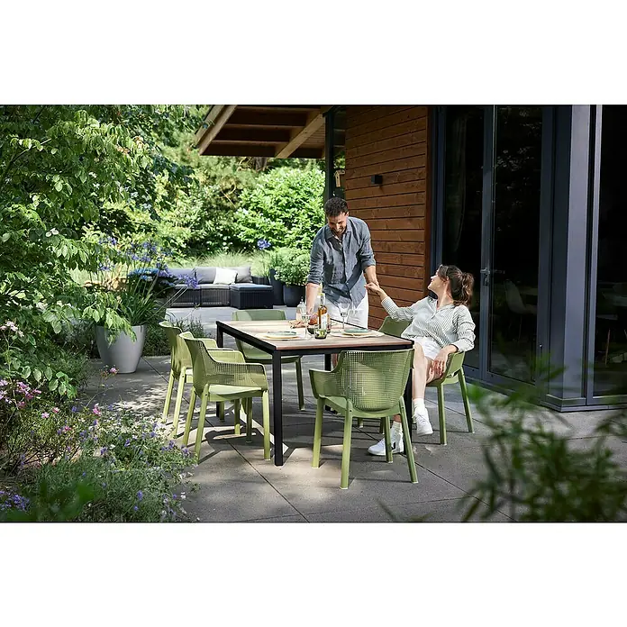 Keter Mesa de jardín Porto - L x An x Al: 155 x 95 x 75 cm, Polipropileno, Rectangular, Walnut/Antracita - Escena al aire libre con mesa de comedor y sillas verdes, donde un hombre y una mujer están sentados hablando. La mesa está puesta para comer.