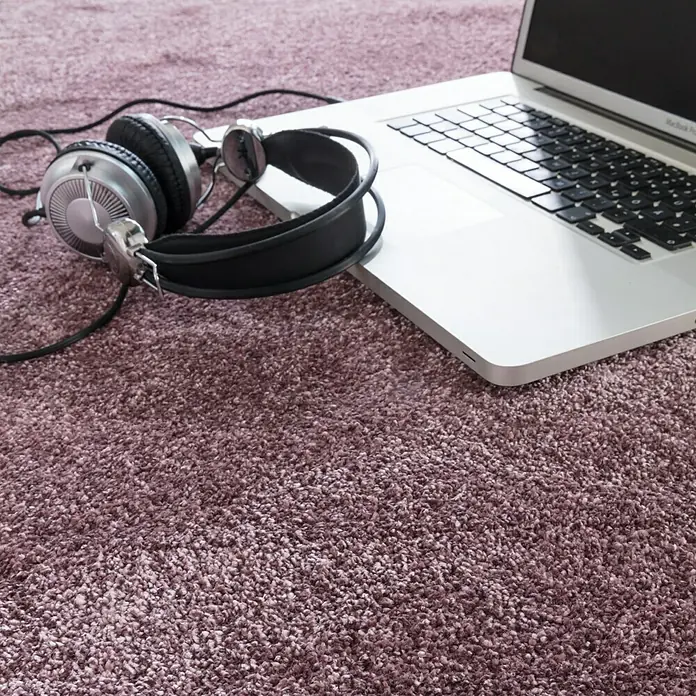 Kurzflorteppich SofttouchPastell-Lila, 290 x 200 cm, 100 % Polypropylen (Flor) - Laptop und Kopfhörer auf einem Teppich. Die Kopfhörer sind silberfarben und haben ein schwarzes Kopfband. Der Teppich ist lila.