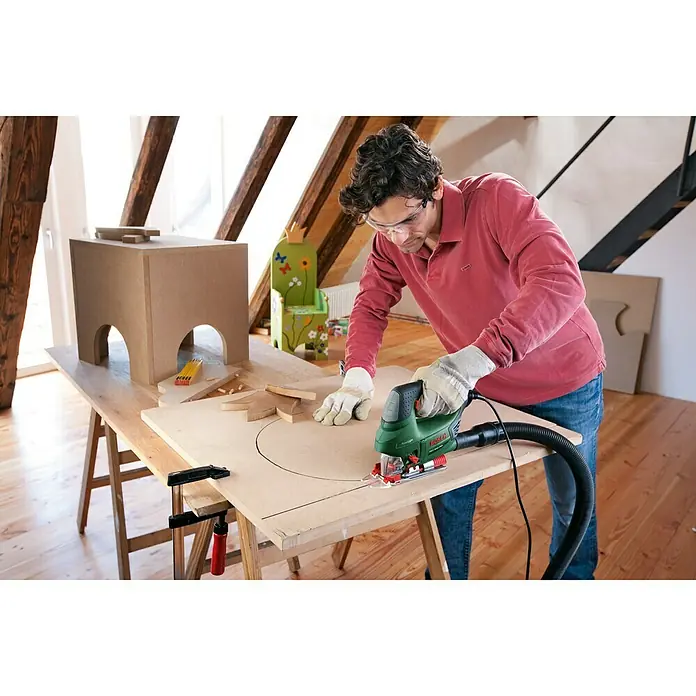 Bosch Elektro-Pendelhubstichsäge PST 900 PEL - 500 /min - 3.100 /min, Max. Schnitttiefe in Holz: 90 mm, Anzahl Pendelhubstufen: 4 Stk. - Mann sägt mit einer Bosch Stichsäge ein Brett. Die Stichsäge ist grün und schwarz.