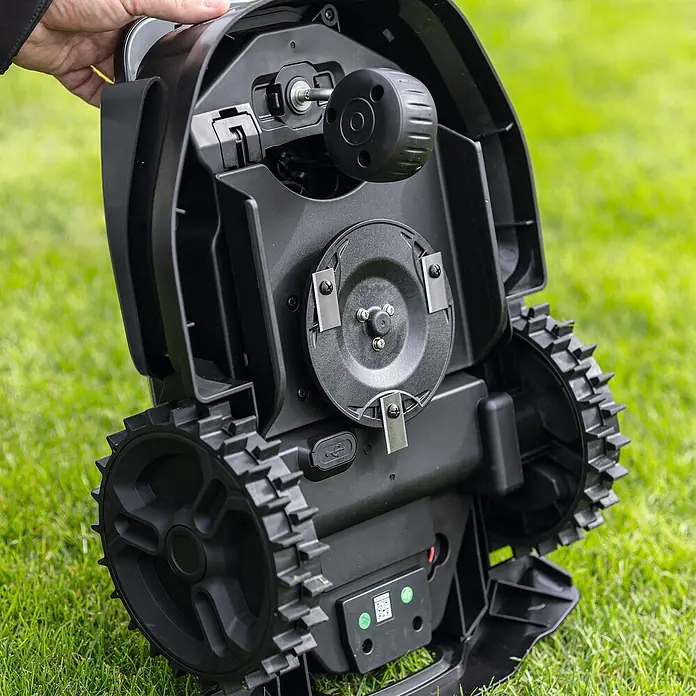 Scheppach Mähroboter RRMA300 - Max. Flächenempfehlung: 300 m², Schnittbreite: 160 mm, Begrenzungskabel - Ein detailreiches Bild der Unterseite eines Rasenmähroboters, der auf einem grünen Rasen steht. Die scharfen Klingen und robusten Räder sind gut sichtbar.