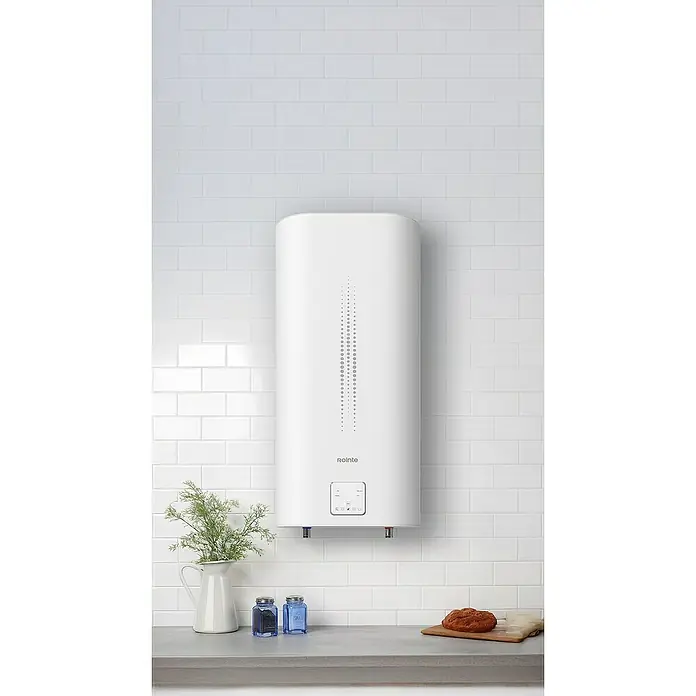 Rointe Termo eléctrico Luxe Slim - 100 l, 2.000 W, Montaje en la pared - Primer plano de un calentador de agua blanco Rolinte montado en una pared de ladrillo blanco. Elementos decorativos colocados en la encimera.