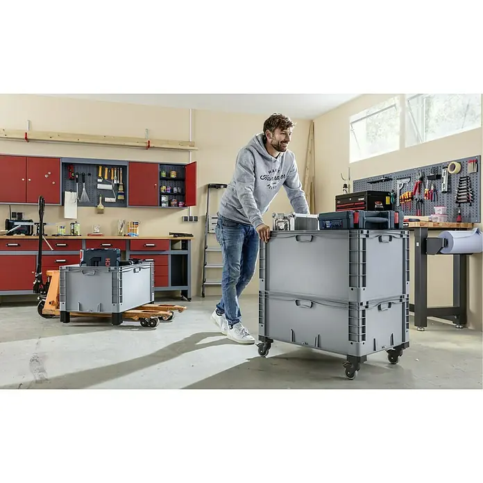 Surplus Systems Deckel - Passend für: Surplus Systems Euronormbox 80 x 60 cm, L x B: 80 x 60 cm - Ein Mann steht neben zwei robusten grauen Lagerboxen auf Rollen, ideal für Werkstatt oder Lager, die Ordnung und Mobilität bieten.