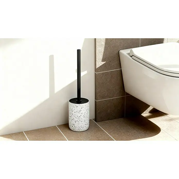 Camargue WC-Bürstengarnitur Stone Terrazzo - B x H: 9,6 x 39,5 cm, Polyresin, Weiß/Schwarz - Aufnahme einer WC-Bürste mit schwarzem Griff und weißem Behälter mit Sprenkeln, stehend in einem Badezimmer mit Fliesen und einer Toilette.
