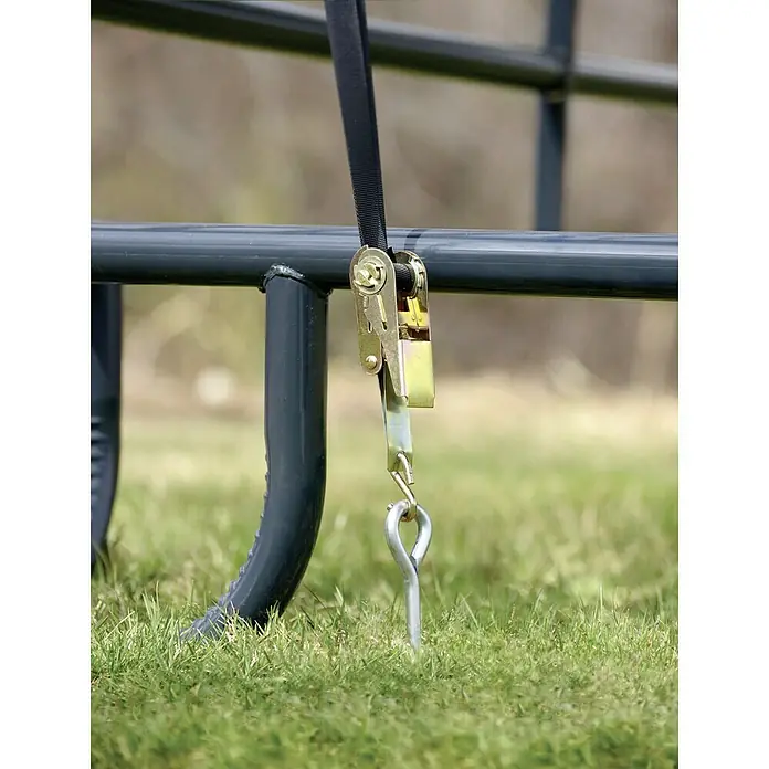 ShelterLogic Weidezelt - Grundfläche: 13,7 m², Kunststoff - Detailaufnahme eines Spannriemens, der an einem Metallrahmen befestigt ist und mit einem Erdanker im Gras fixiert wird.