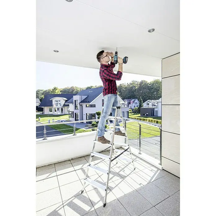 Krause Monto Doppel-Stehleiter Dopplo - Arbeitshöhe: 3,05 m, Anzahl Tritte: 14 Stk., Belastbarkeit: 150 kg, Aluminium - Mann auf einer Leiter, der mit einem Akkubohrer eine Deckenleuchte befestigt. Der Akkubohrer ist blau und schwarz.
