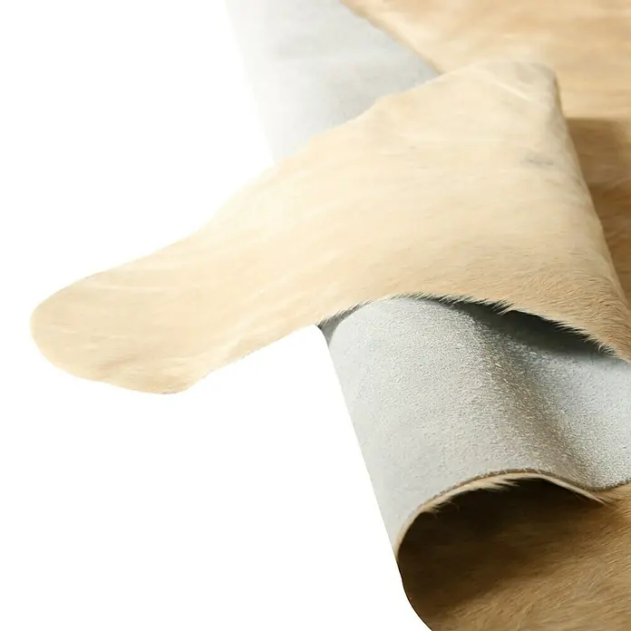 Esbeco Kuhfell - Exotisch Hell, 100 % Echtfell - Nahaufnahme eines beigen Kuhfellteppichs, der seine weiche Textur und neutrale Farbpalette hervorhebt. Ideal für rustikale oder moderne Dekore.