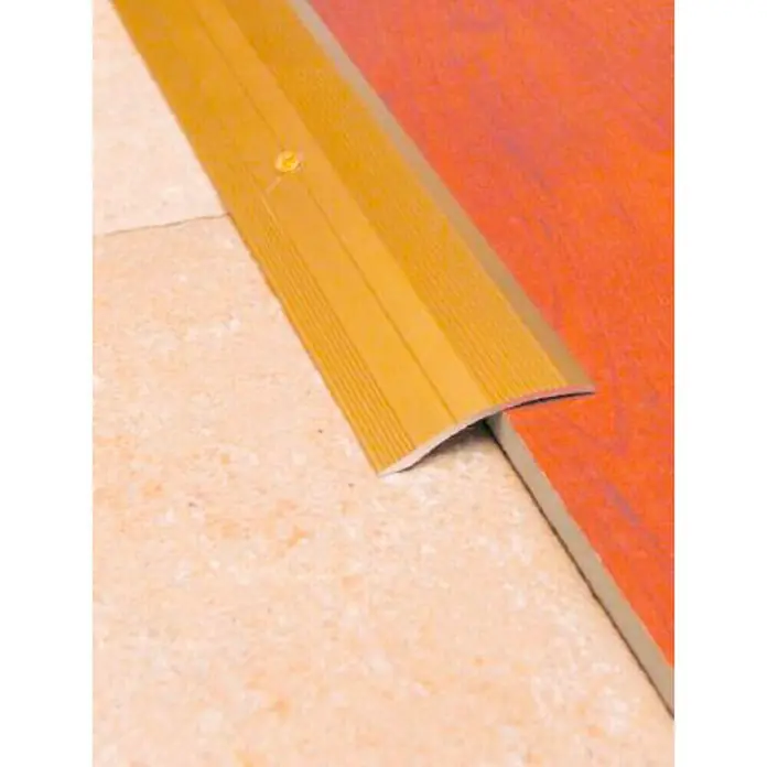 Perfil de transición Oro - Aluminio, Oro, 1 m x 15 mm - La imagen muestra una tira de transición dorada entre dos pavimentos diferentes, proporcionando un acabado limpio y pulido.